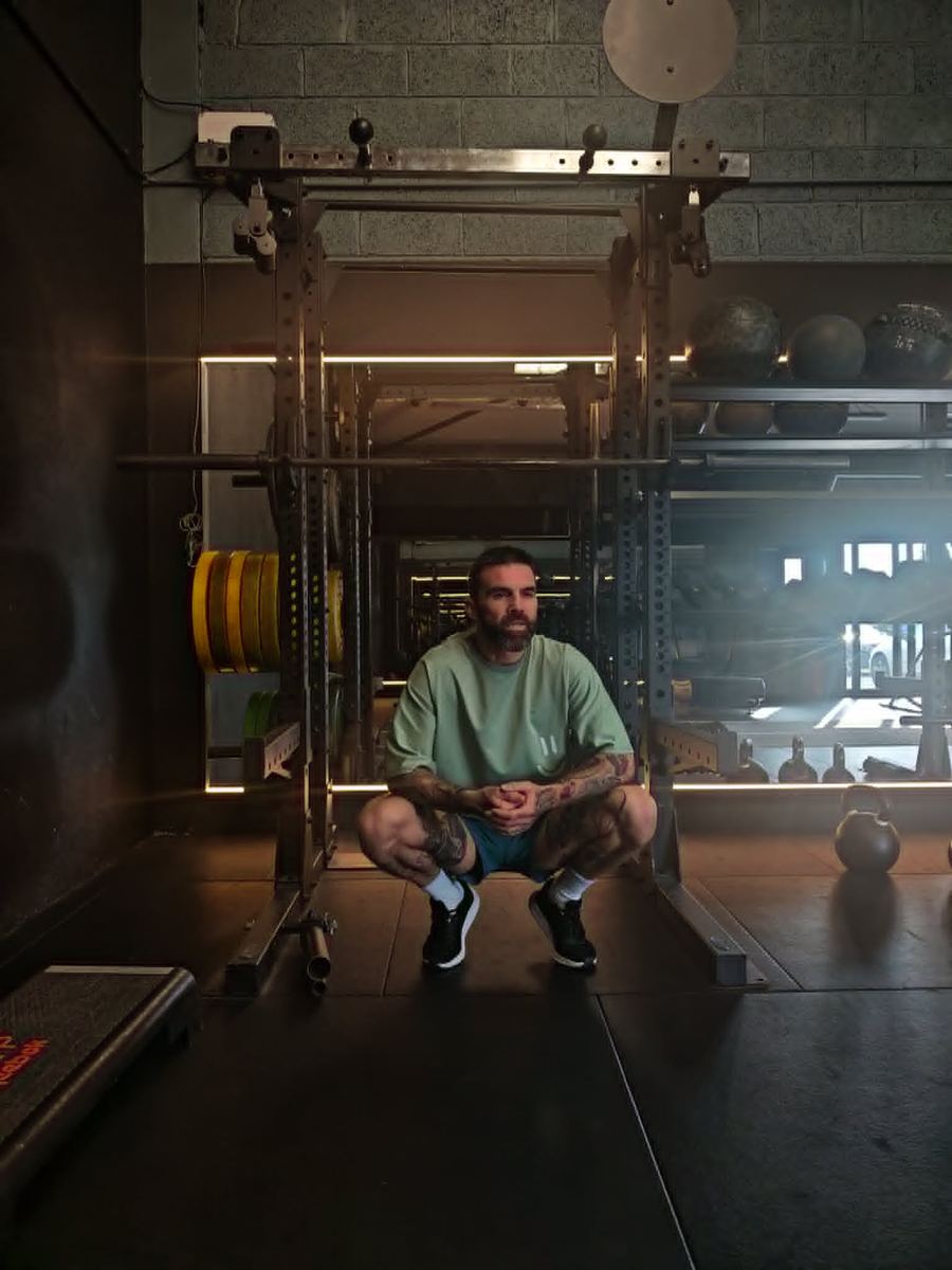 Ian Wilson, personal trainer, sitting in a squat rack at the gym