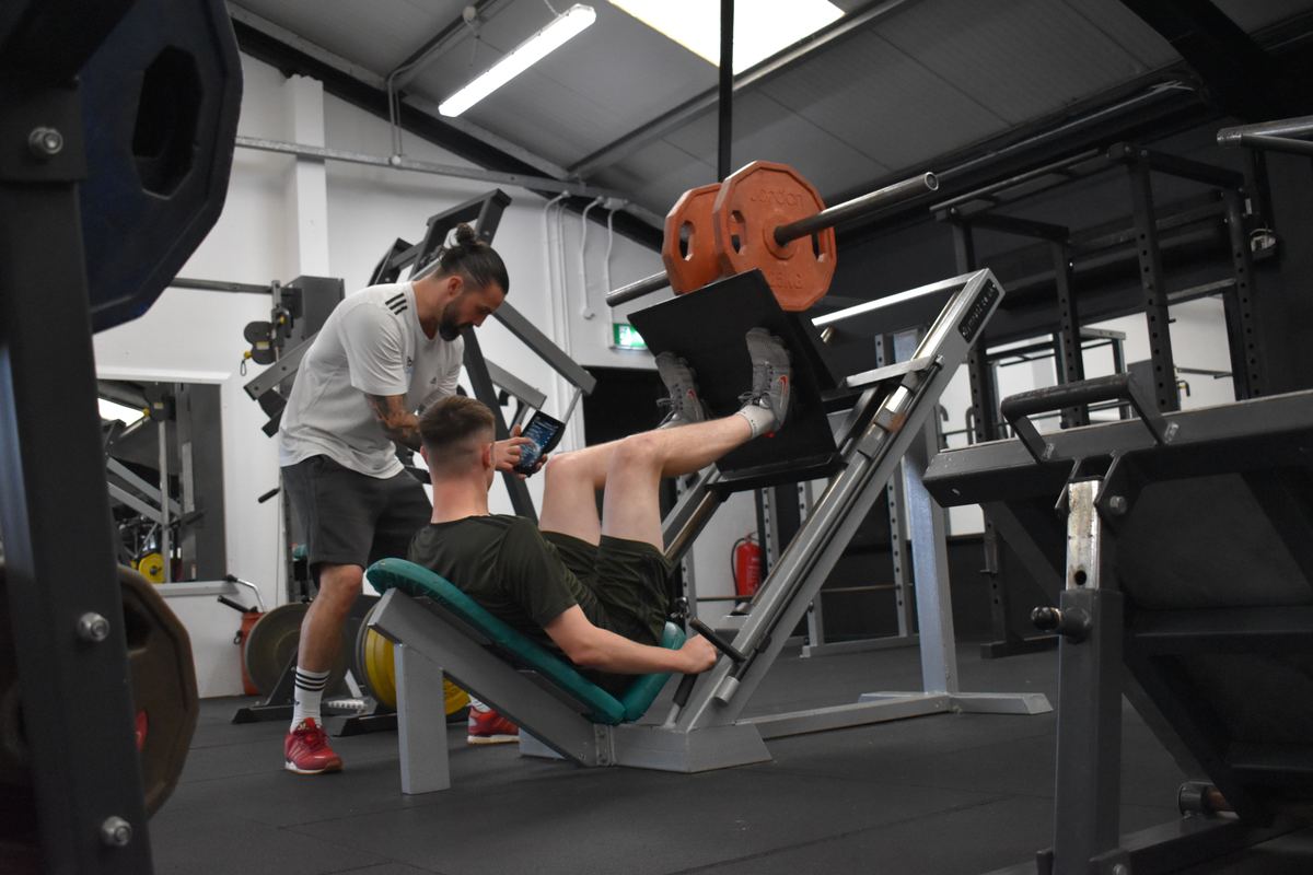 Ian Wilson showing a client their programme on a device during a leg press set