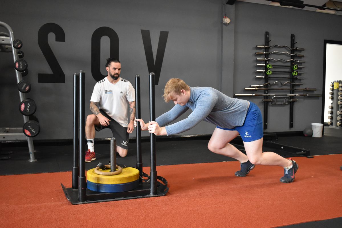 A client pushing a weighted sled while Ian Wilson coaches alongside